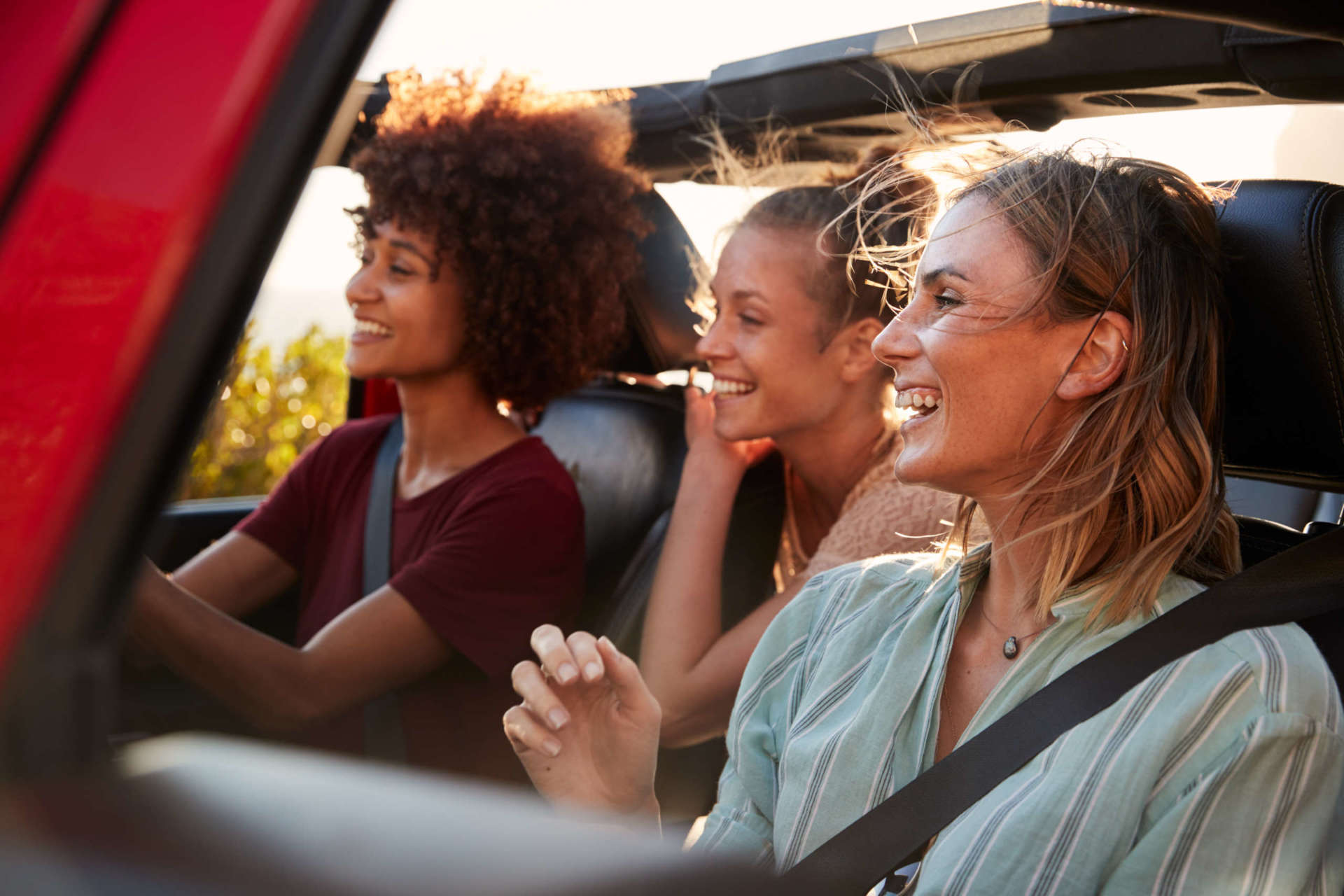 Three millennial female friends on a road trip driving together in an open jeep, close up auto insurance by fero & sons