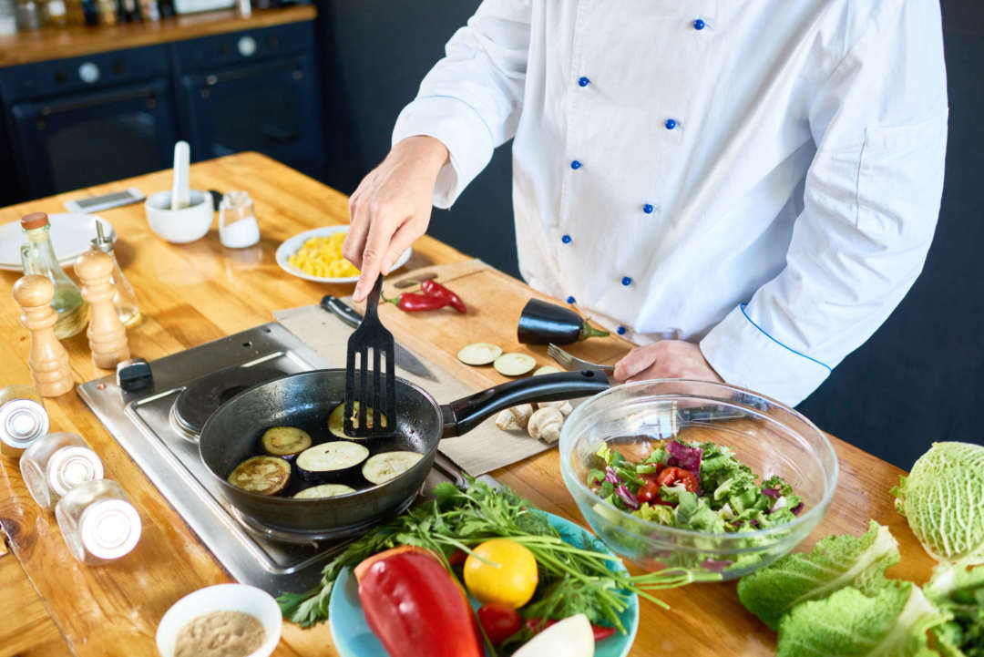 A chef frying eggplant in a pan and preparing a salad.